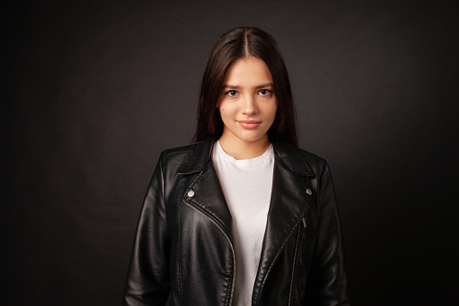 Studio portrait of a teenage girl in a black leather jacket against a black background