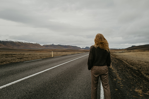 View from behind on woman standing on the road in Iceland with her hair moving on the wind