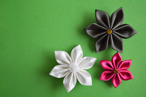 Kanzashi flowers on green background with copy space. Handmade fabric flowers. Hobby and craft concept.