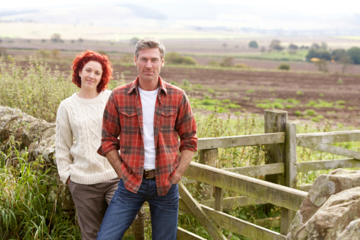 Couple in countryside standing by wooden gate smiling at camera