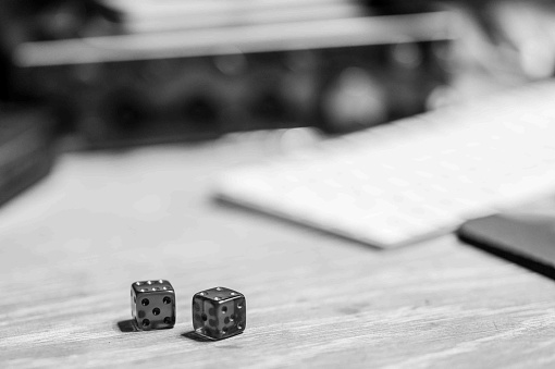 Black and white photo of dice in top of a desk with equipment in background