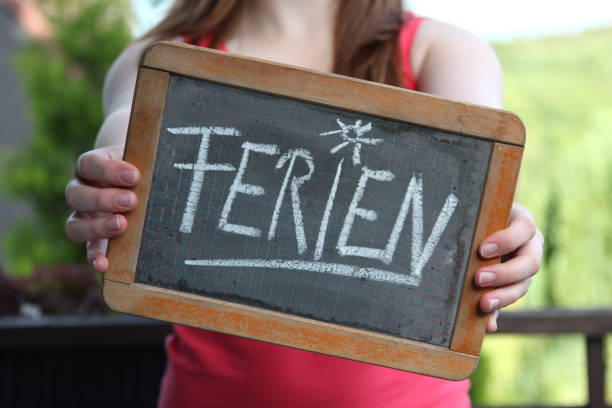 istock Ferien (vacation in German language) written with chalk on slate shown by young female 1771219412