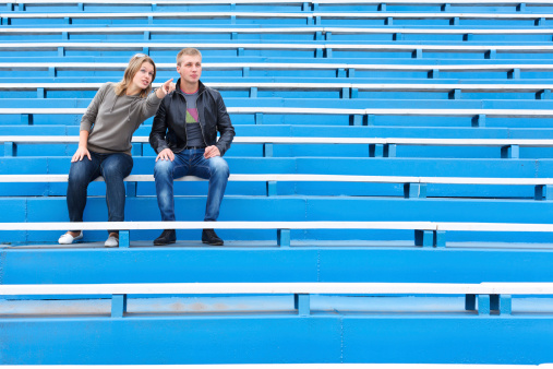 Man and woman sitting together on empty sports tribune. Blue sits