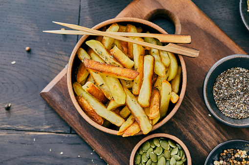 French fries, with natural herbs and spices, served  on a black plate, bar, restaurant or home, dark mood rustic wooden kitchen black table background, close up view with copy space, representing fast food and city life, indulgence and joy through gourmet streetfood lifestyle
