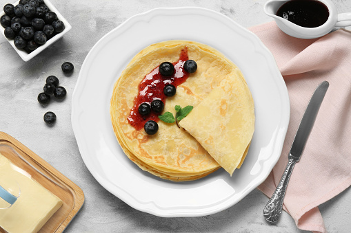 Delicious crepes with blueberries, mint and jam on light grey table, flat lay