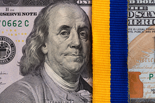 US 100 dollar banknotes with ukrainian flag colors ribbon for design purpose