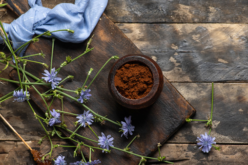 Chicory powder in a wooden jar and wild chicory flowers on a wooden table. Dried chicory root used as coffee substitute. Healthy food and drink