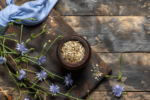 Chicory root in a wooden jar and blue wild flowers on a wooden table. Chicory root is used as a substitute for coffee, and tea can also be prepared from it