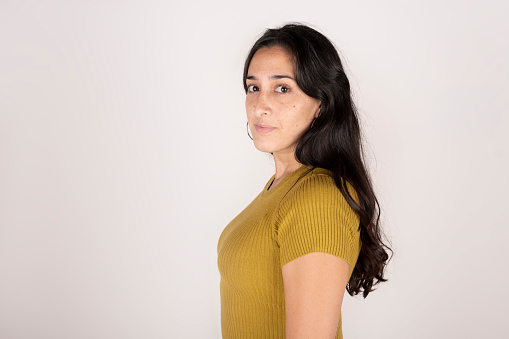 Brunette latin woman standing in profile on white background looking at camera