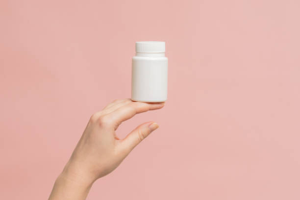 istock Plastic bottle (tube) in hand on pink background. Packaging for vitamins, tablets or capsule, or supplement 1771305629