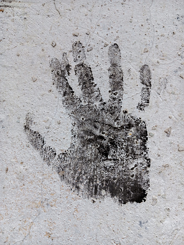 Black paint human handprint on cement wall.