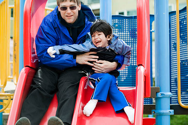 Father going down slide with disabled son stock photo