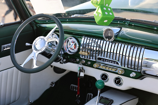 Vintage dashboard of a 1950s sedan with green fuzzy dice hanging from the mirror