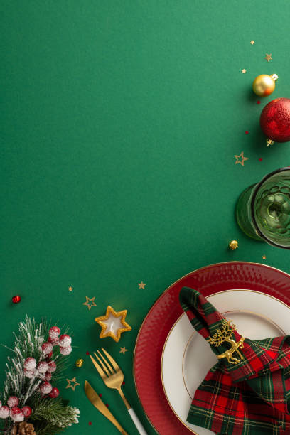 istock Design festive table setting: Top-view vertical image of plate, golden flatware, checkered napkin with ring, glass, balls, natural Christmas tree twigs, candle, glimmering confetti, mistletoe on green 1771352033