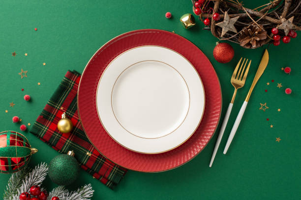 istock Christmas celebration table setup. Overhead shot displaying dishes, gilded cutlery, plaid napkin, baubles, natural wreath, star-shaped confetti, icy fir branches, mistletoe, green backdrop, text area 1771352040