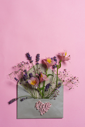 Decorative envelope full of various flowers. Greeting card on a pink background. Love concept, with copy space