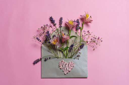 Decorative envelope full of various flowers. Greeting card on a pink background. Love concept, with copy space