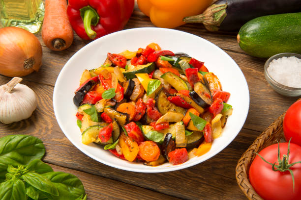 Sautéed  eggplant zucchini carrots and tomatoes in a salad bowl on a rustic wooden table with ingredients. stock photo