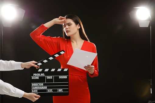 Emotional actress performing role while second assistant camera holding clapperboard on stage. Film industry