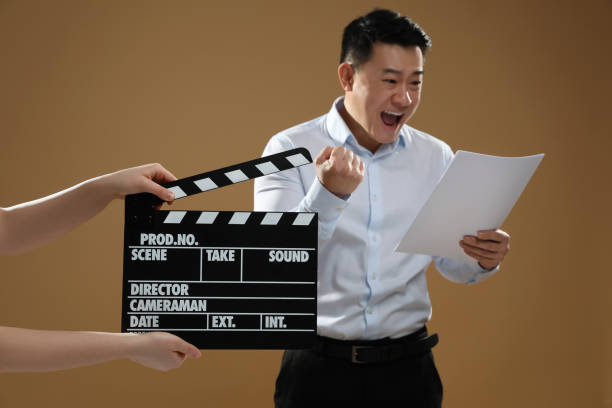 istock Emotional asian actor performing role while second assistant camera holding clapperboard on brown background, selective focus. Film industry 1771394528