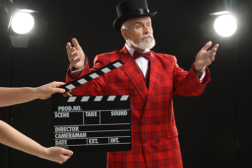 Senior actor performing role while second assistant camera holding clapperboard on stage, selective focus. Film industry