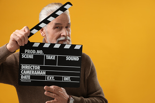 Senior actor holding clapperboard on yellow background, space for text. Film industry