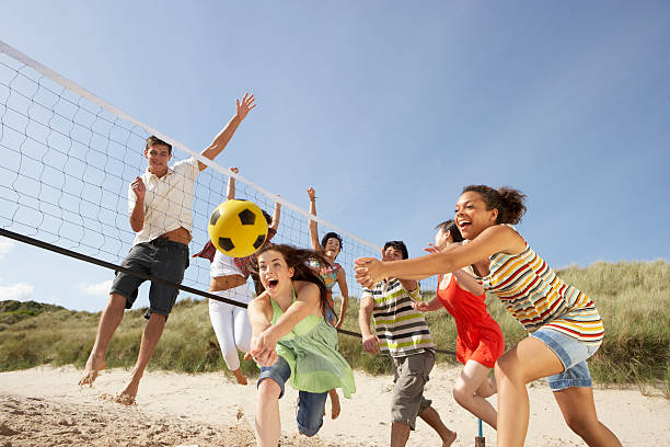 Group of friends playing volleyball on the beach Group Of Teenage Friends Having Fun Playing Volleyball On Beach Together beach play stock pictures, royalty-free photos & images