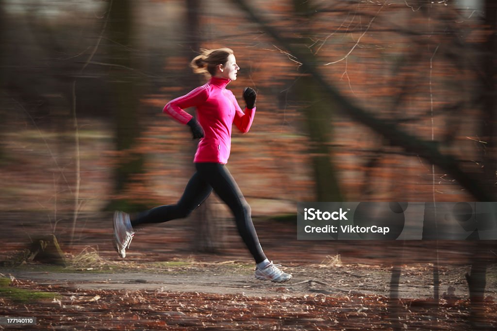 Running woman in focus with blurred woodland background Young woman running outdoors in a city park on a cold fall/winter day (motion blurred image) Active Lifestyle Stock Photo