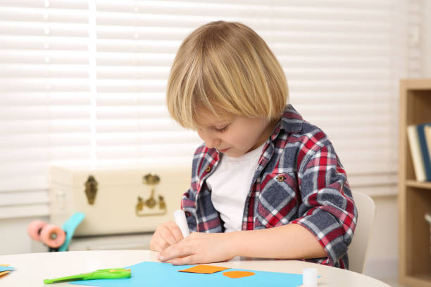 istock Cute little boy using glue stick at desk in room. Home workplace 1771419802
