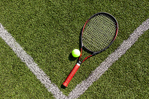 professional tennis racket with ball lies on green court, tennis equipment on the floor, close-up