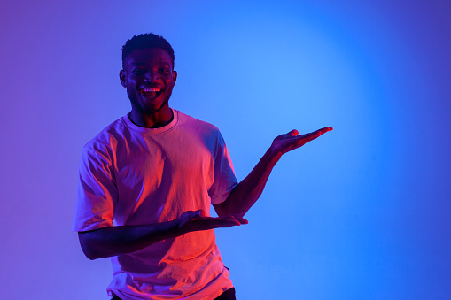 african american man shows his hands to the side in neon lighting, the guy smiles and advertises copy space