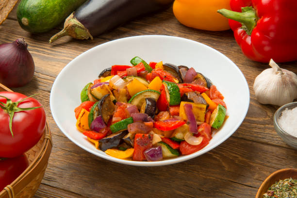 Ratatouille salad in a porcelain salad bowl on a rustic wooden table with ingredients. stock photo