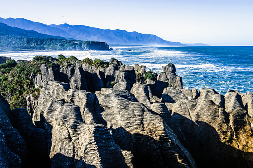 View of eroded rocks forming sheets on Pancake Rocks beach, in mid-morning light. In the background you can see the beach. Punakaiki, West Coast of the South Island in New Zealand