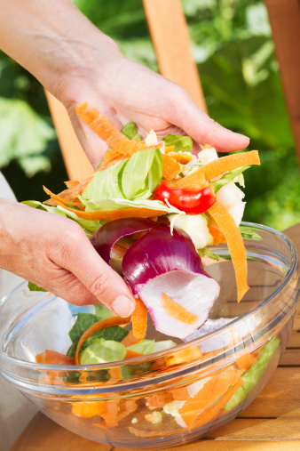 Close-up of kitchen fruit and vegetable scraps being placed into a glass bowl ready for transfer to a composting bin.