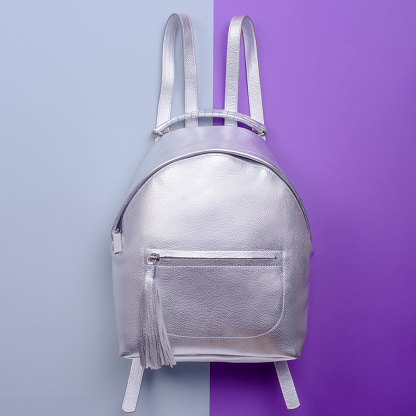 Modern silver metallic leather backpack for women with a handle and a zippered pocket with a tassel pull isolated on a two-color background. Mockup for product advertising. Fashion photography.