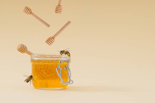 istock Creative layout made with honey dippers falling into jar full of natural honey and honeycombs and honey bees flying around on light cream background. Minimal nature concept. Trendy healthy food idea. 1771521243