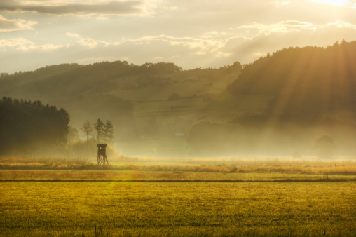 Glorious morning on the Austrian countryside. Bright golden sun rays bursting through the clouds onto a misty field.