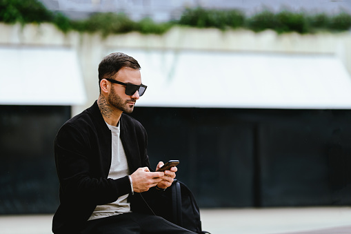 stylish young man in sunglasses using mobile phone outdoors.