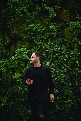 young man in a black clothes in front of a green plant wall.