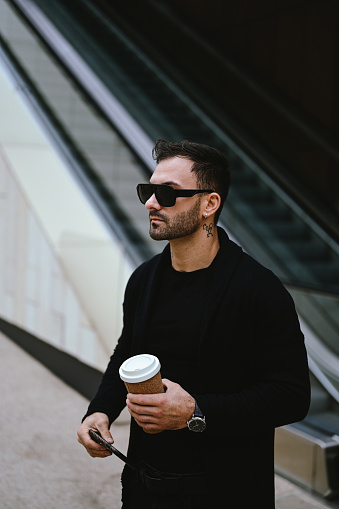 stylish man in. black sunglasses and coffee cup waiting on a street.