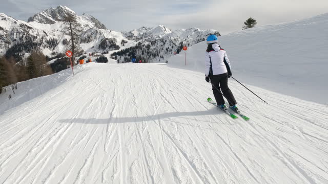 Following unknown lady skiing on groomed ski track at picturesque alpine resort