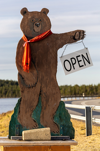 Inari, Finland Oct 7, 2023 A figure of a large bear on the side of the road near a lake holds a sign saying Open for a local attraction.