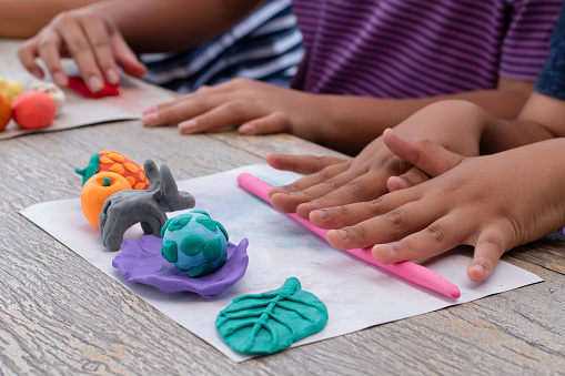 Children with learning disabilities are practicing plasticine shapes such as animals and fruits on the table with friends. Idea for learning by doing for children with learning disabilities.