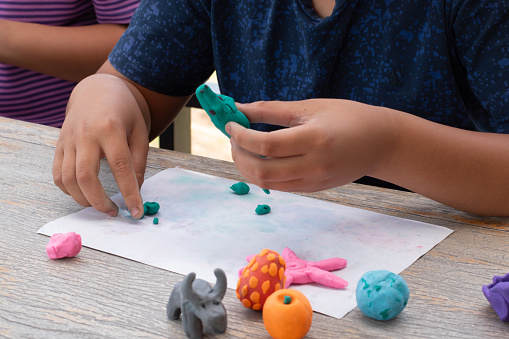 Children with learning disabilities are practicing plasticine shapes such as animals and fruits on the table with friends. Idea for learning by doing for children with learning disabilities.