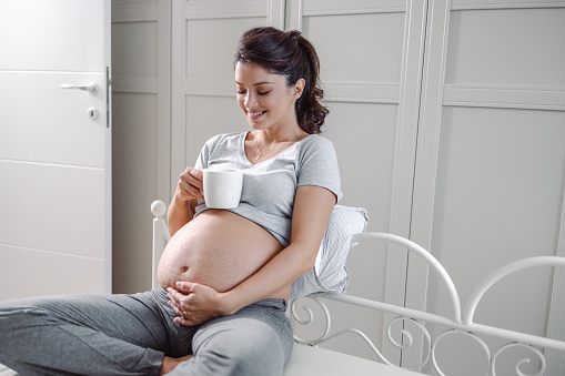 Beautiful pregnant woman holding her belly and enjoying in bed. Happy maternity and pregnancy concept