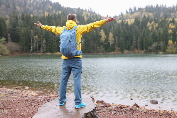 istock Man spreads hands to sides standing on stone against lake 1771692171