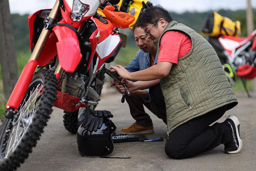 Two men are working together to solve a motorcycle problem while on a motorcycle camping trip