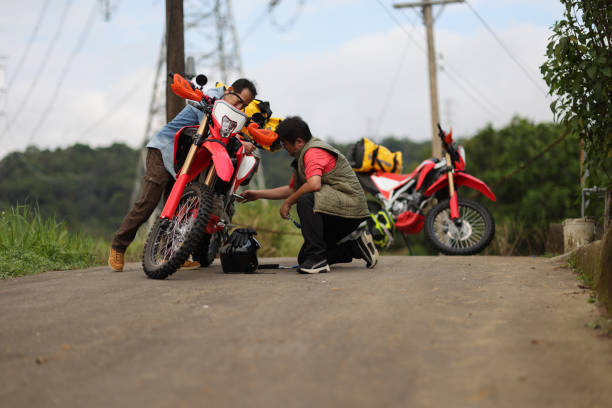 Two men are working together to solve a motorcycle problem while on a motorcycle camping trip