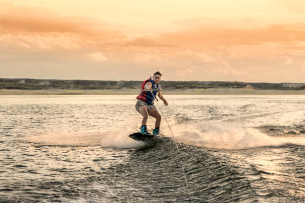 молодые люди, практикующие вейкбординг, на озере на закате. - wakeboarding waterskiing water ski sunset стоковые фото и изображения