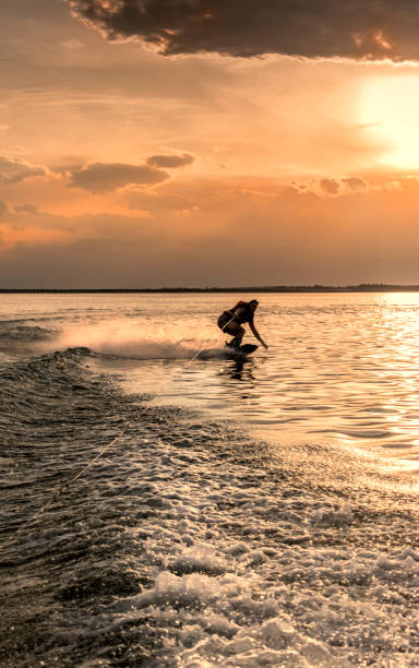 Young adult practicing wakeboarding, on lake at sunset.